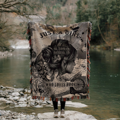 A person is standing on a rock, holding a blanket that features a book-themed design, with a river and trees in the background.