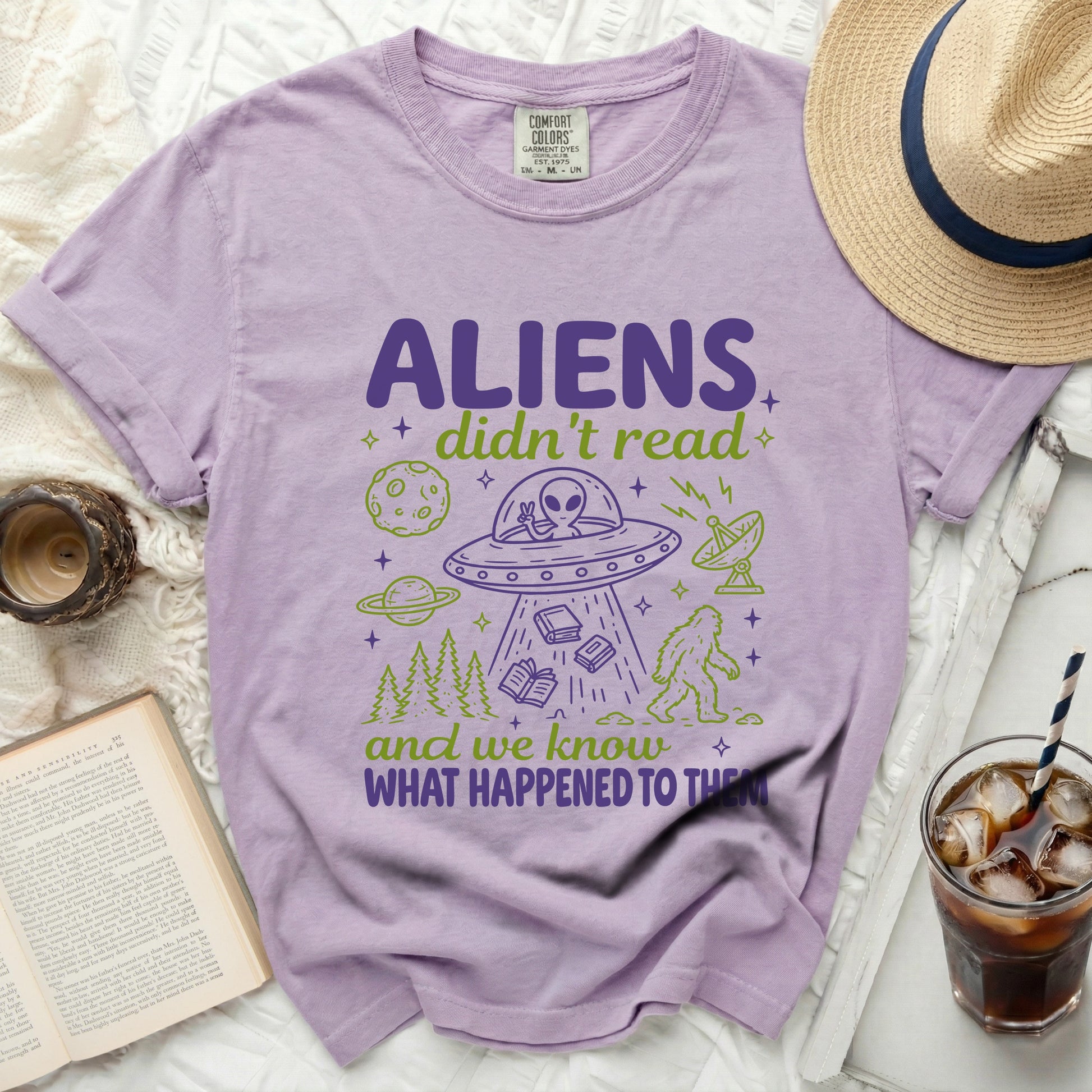 Lavender t-shirt with purple and green print of aliens, UFO, books, and Bigfoot.