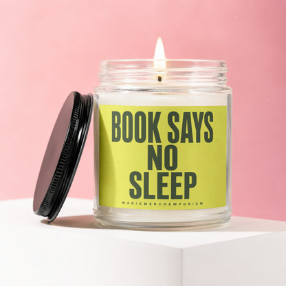 Glass candle with lid off, burning flame, and bright green label reading "BOOK SAYS NO SLEEP".