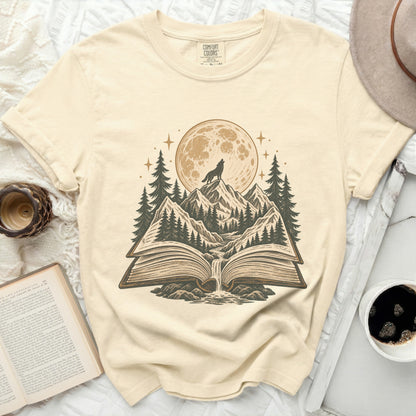 Cream t-shirt with graphic of wolf howling at moon over mountains from an open book.