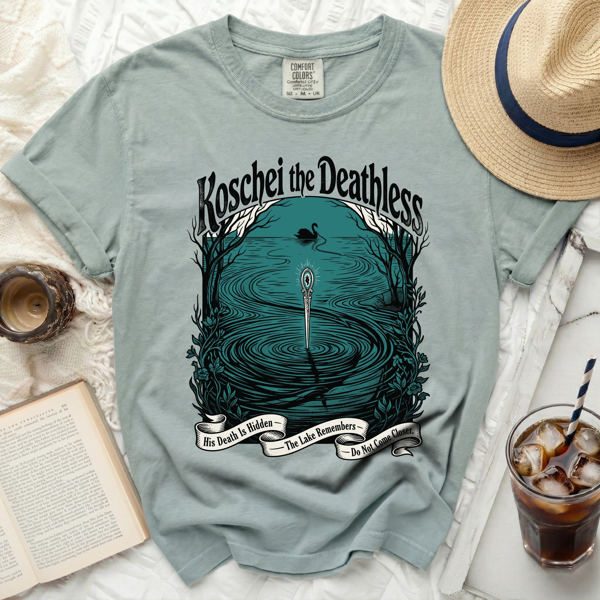 Light blue t-shirt with "Koschei the Deathless" and a lake scene with a swan.