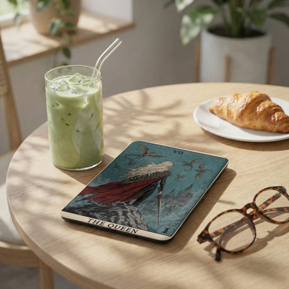 Tarot card "The Queen" with dragons and castle, next to matcha drink and croissant.