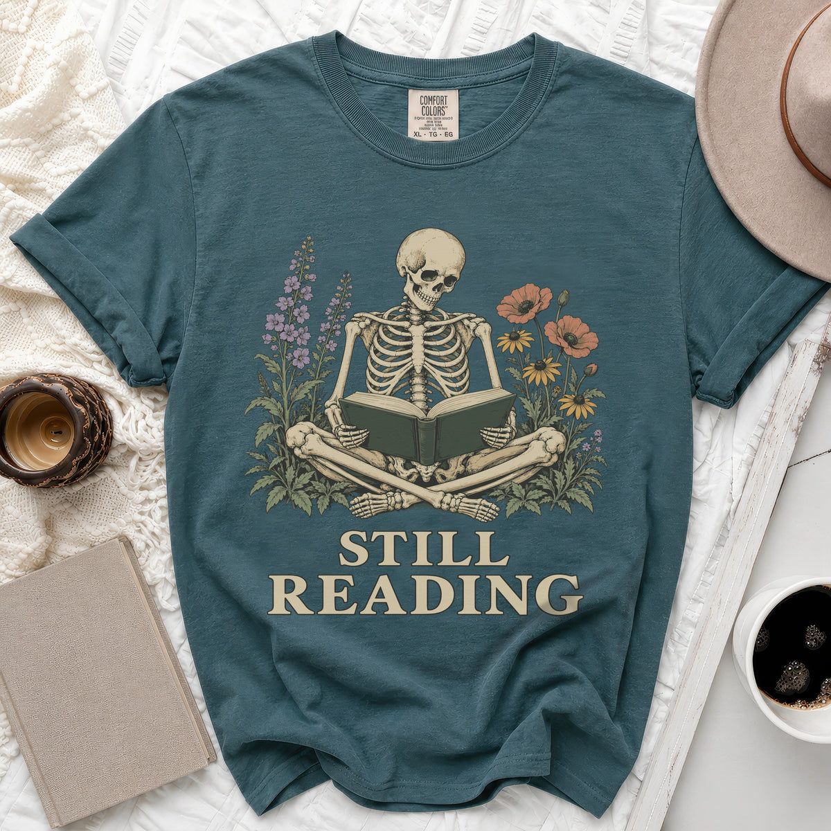 Skeleton reading a book surrounded by flowers with text "STILL READING".