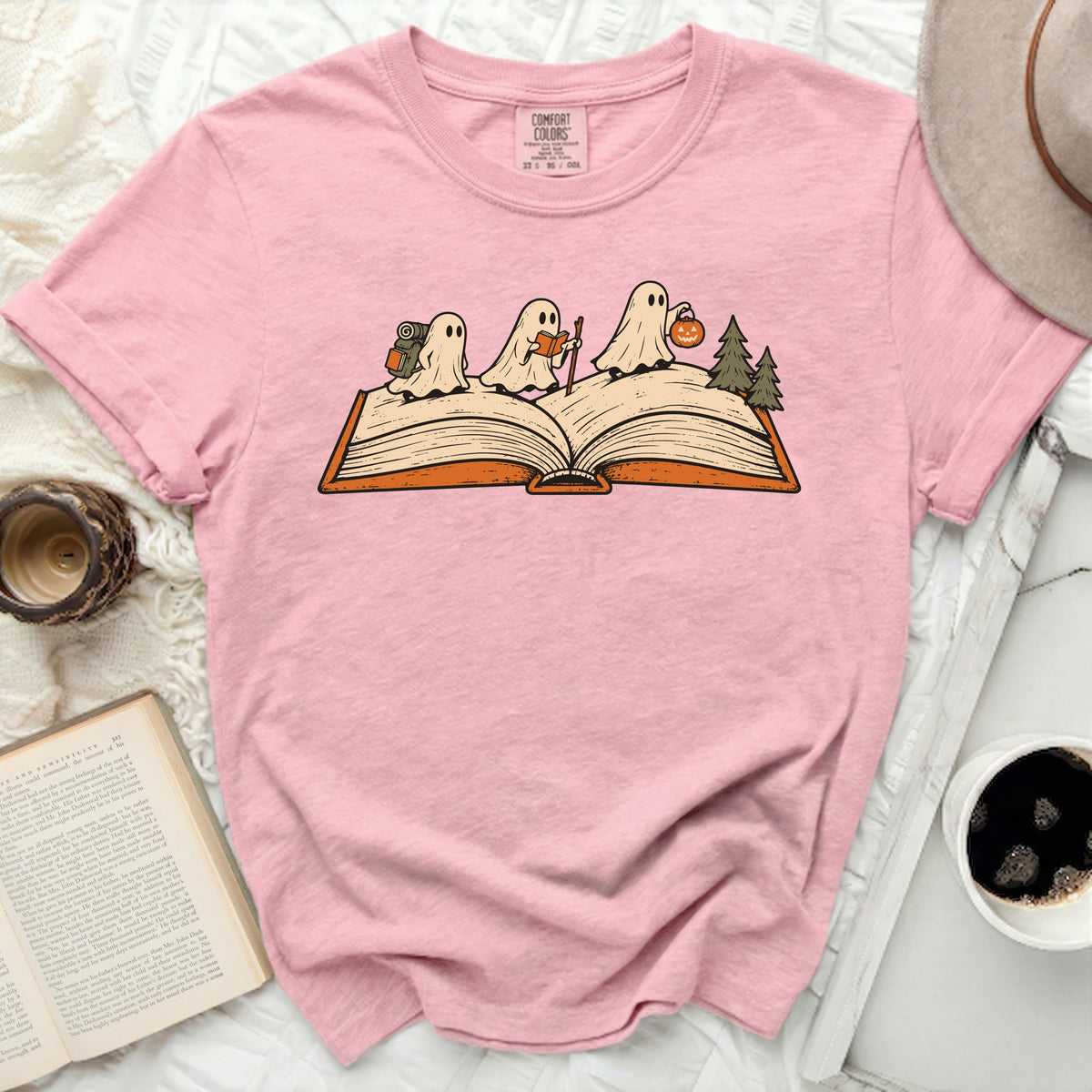 Pink t-shirt with three ghosts on an open book, one with a backpack.