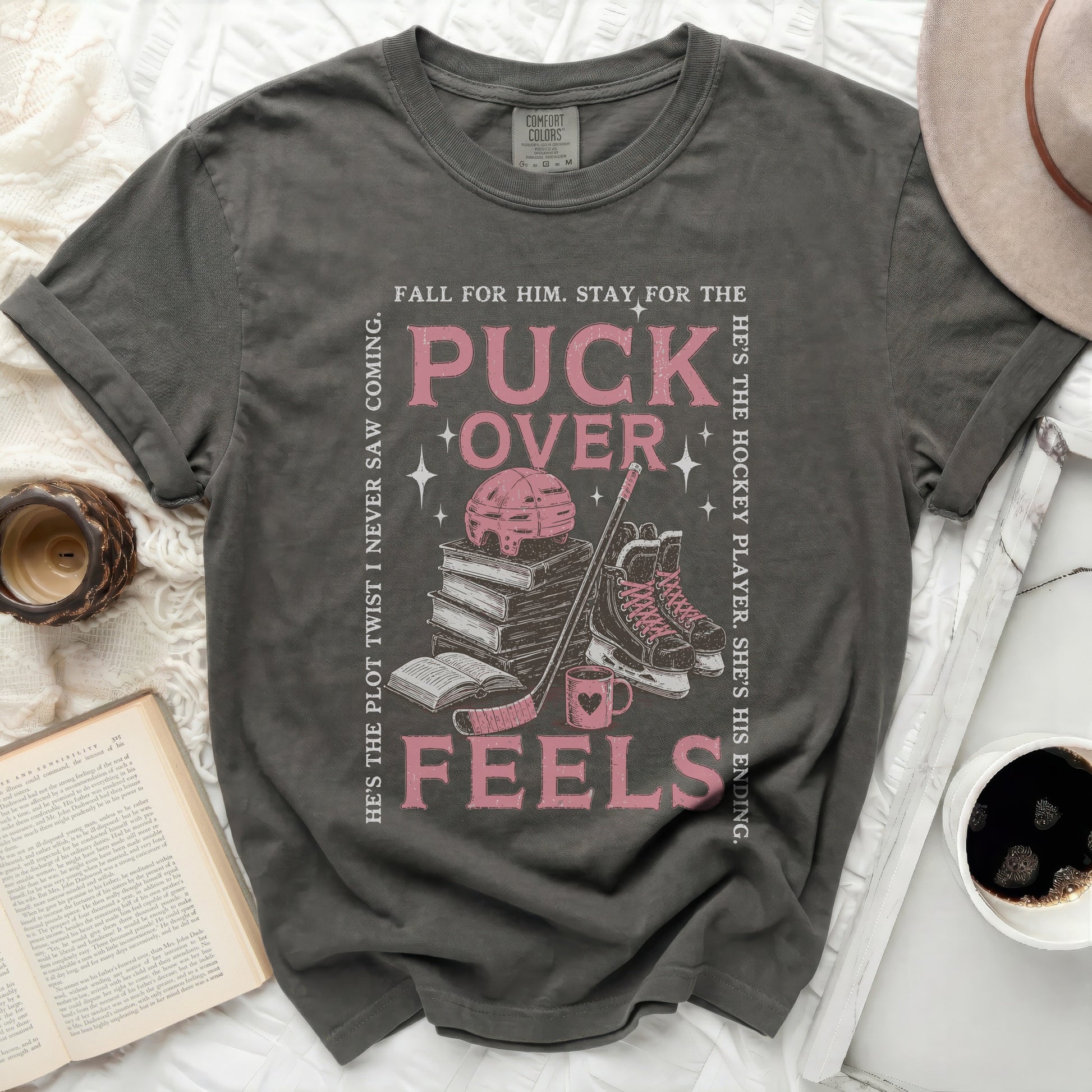 Dark grey t-shirt with "Puck Over Feels" text, books, hockey skates, and puck.