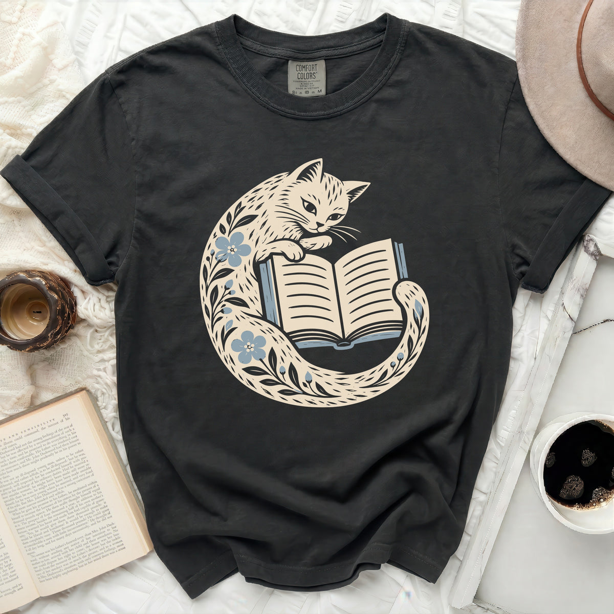 Black t-shirt with a cream cat reading a book surrounded by blue flowers.