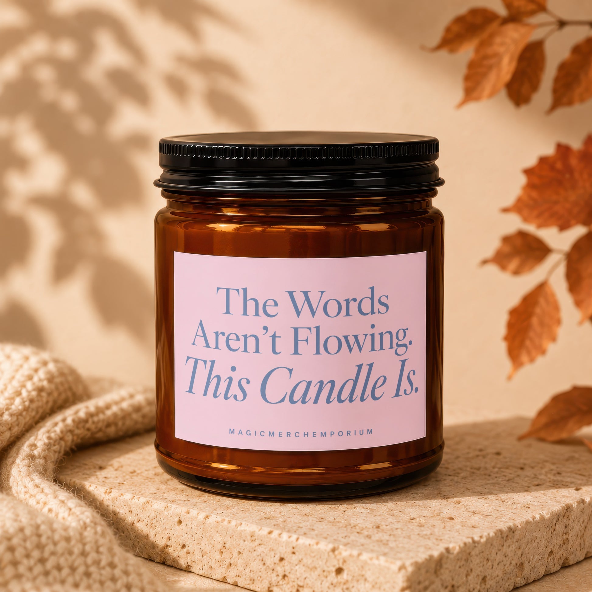 Brown glass candle with pink label reading "The Words Aren't Flowing. This Candle Is."