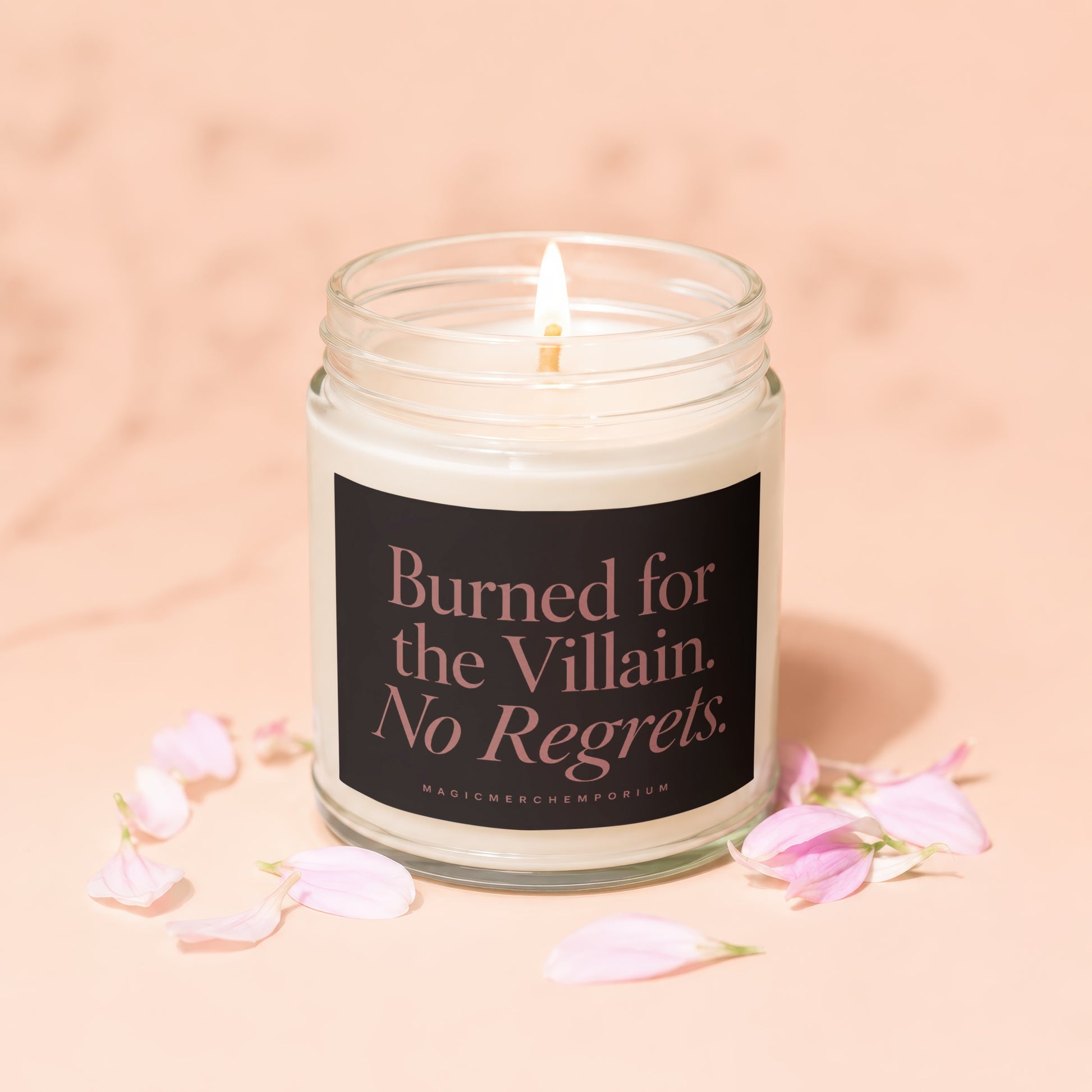 Soy candle with lit wick, dark label text reads "Burned for the Villain. No Regrets."