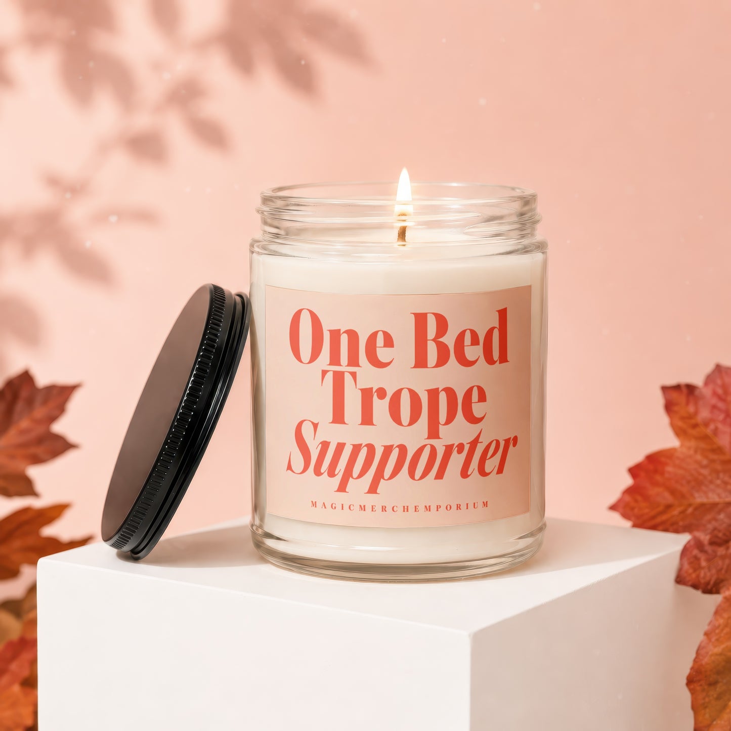 Lit candle in glass jar with "One Bed Trope Supporter" label, lid removed.
