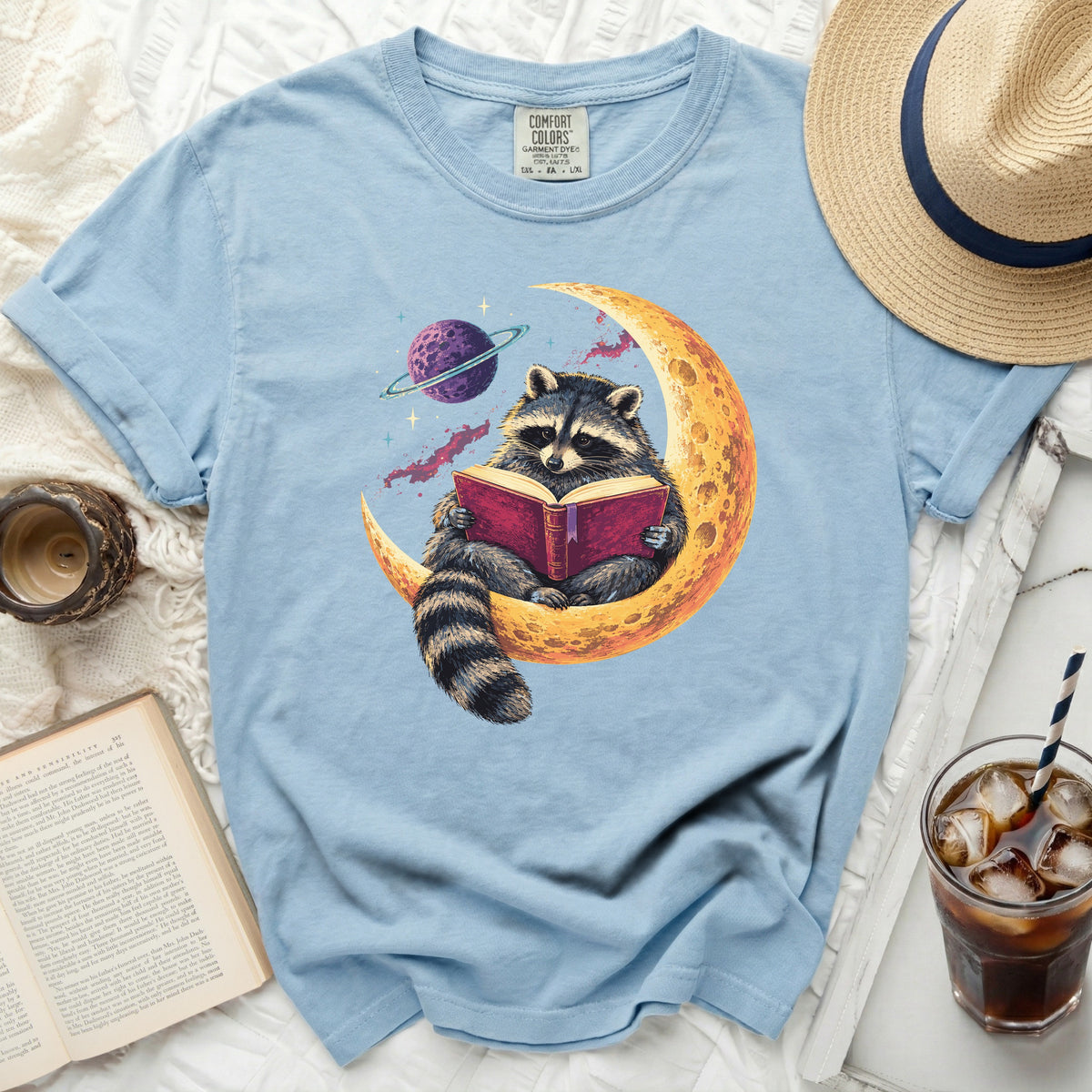 Light blue t-shirt with raccoon reading book on crescent moon graphic.
