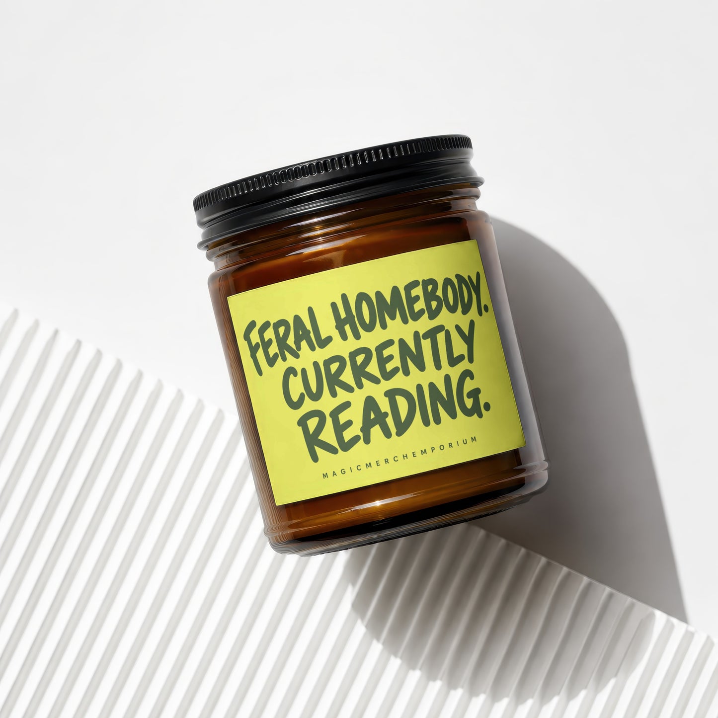 Amber jar candle with yellow label reading "Feral Homebody. Currently Reading."