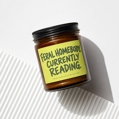 Amber jar candle with yellow label reading "Feral Homebody. Currently Reading."
