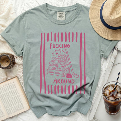 Green t-shirt with pink hockey romance graphic: puck, stick, helmet, books.