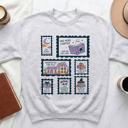 Light gray crewneck sweatshirt with stamp-like graphics featuring spooky and book-themed designs.