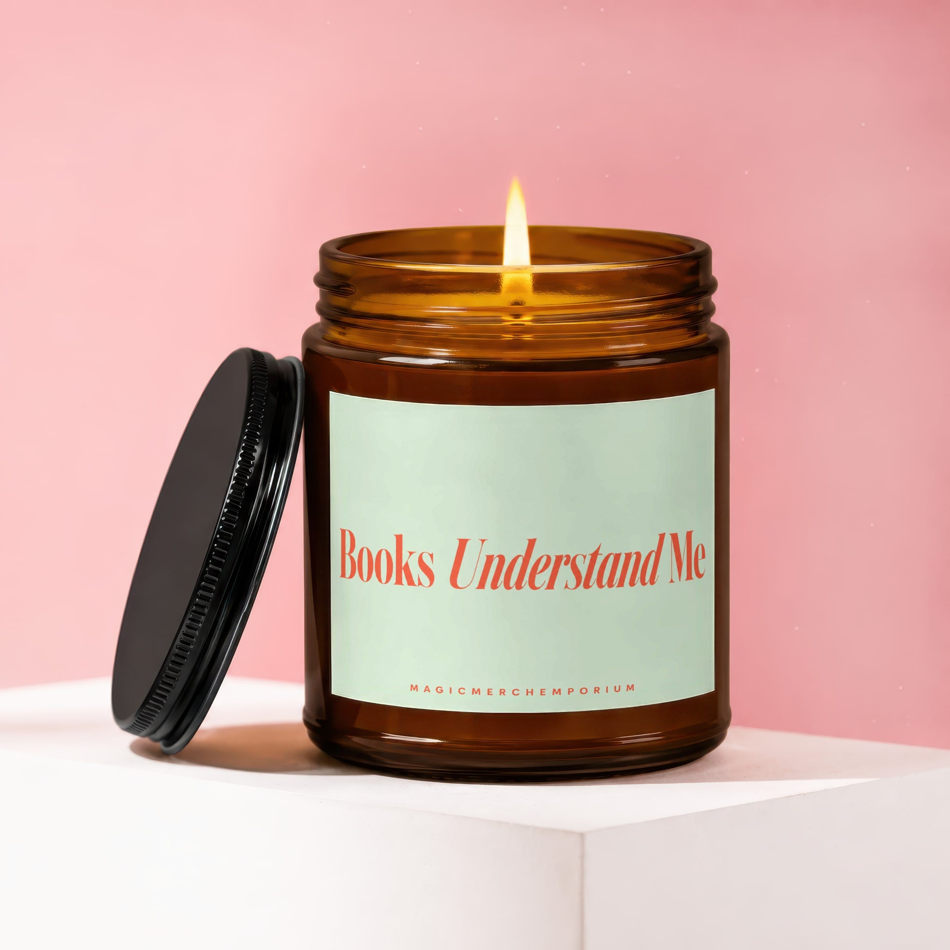 Amber candle with lit wick, lid off, and label reading "Books Understand Me".