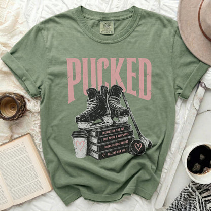 Green t-shirt with "PUCKED" graphic, ice skates, books, and coffee.