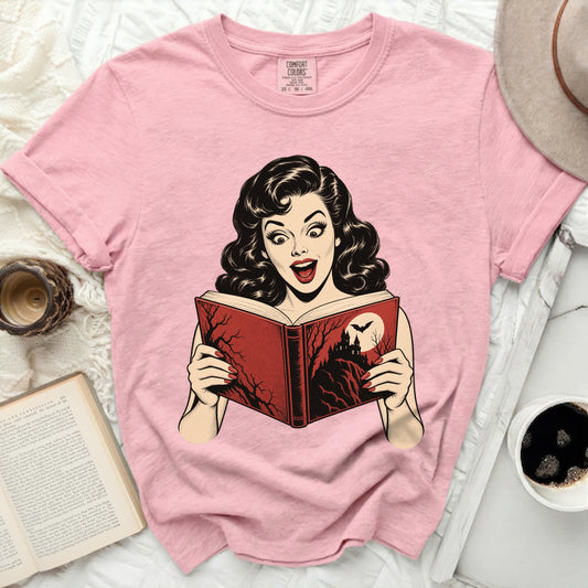 Pink t-shirt with a graphic of a surprised woman reading a spooky book.