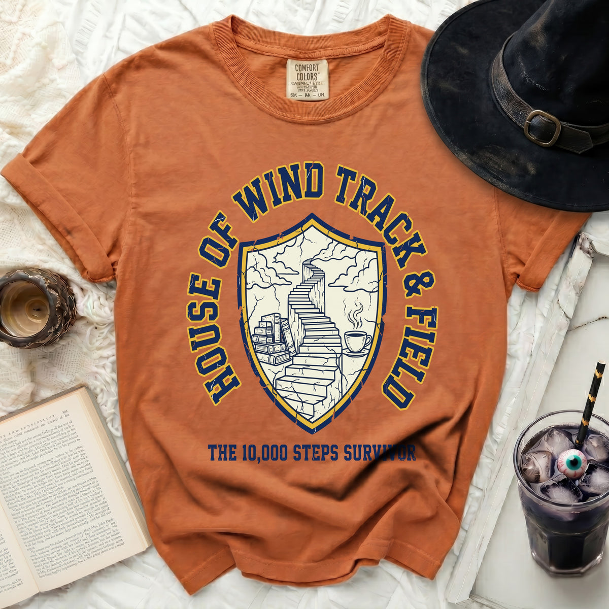 Orange t-shirt with a crest featuring stairs, books, and coffee.