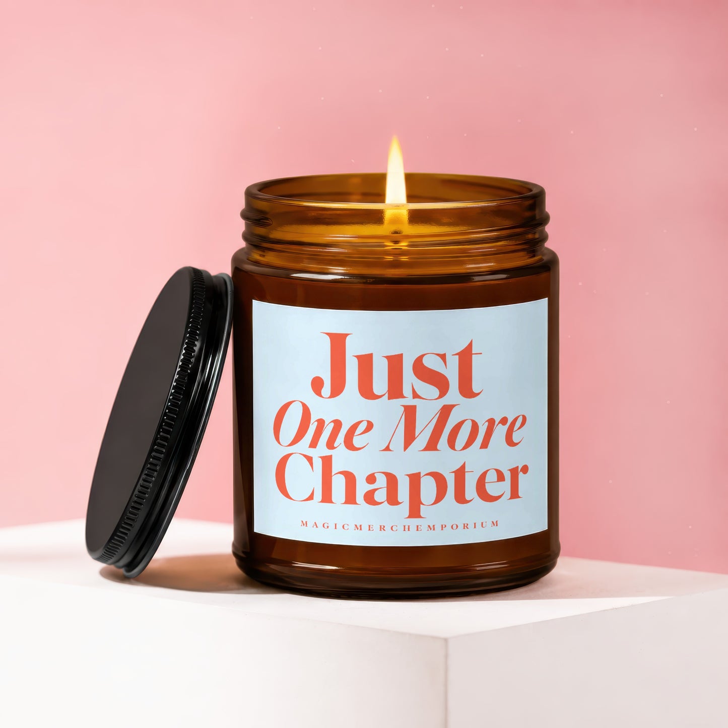 Lit amber glass candle with "Just One More Chapter" text.