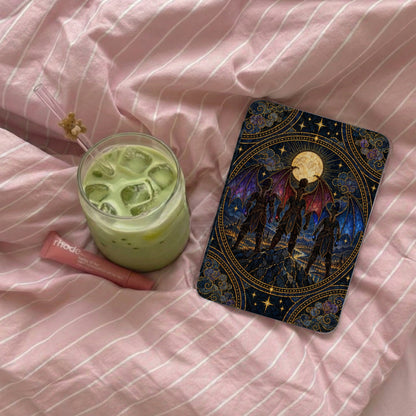 An e-reader with an ornate fantasy art case rests on pink striped bedding next to an iced matcha latte and lip balm.