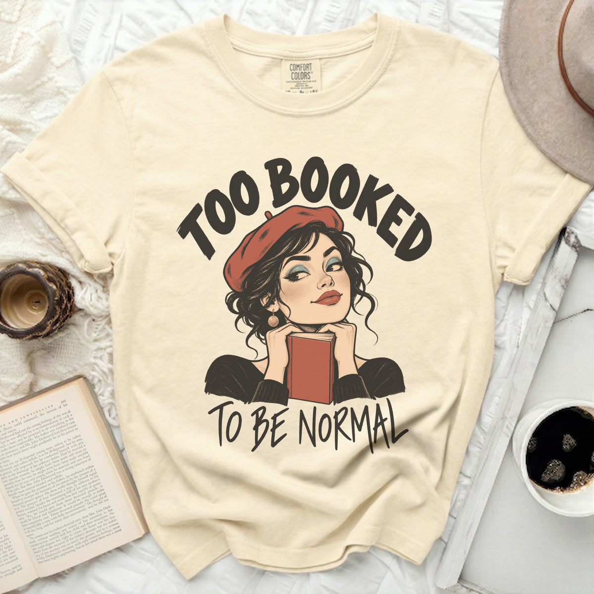 Cream t-shirt with "Too Booked To Be Normal" graphic featuring a woman with a book.