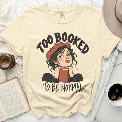 Cream t-shirt with "Too Booked To Be Normal" graphic featuring a woman with a book.