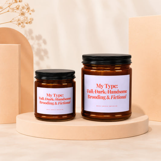 Two amber glass candles with black lids, reading "My Type: Tall, Dark, Handsome Brooding & Fictional".