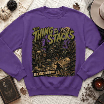 Purple sweatshirt with a graphic of a monster in a library and the text "THE THING IN THE STACKS" and "IT DEVOURS EVERY WORD!".