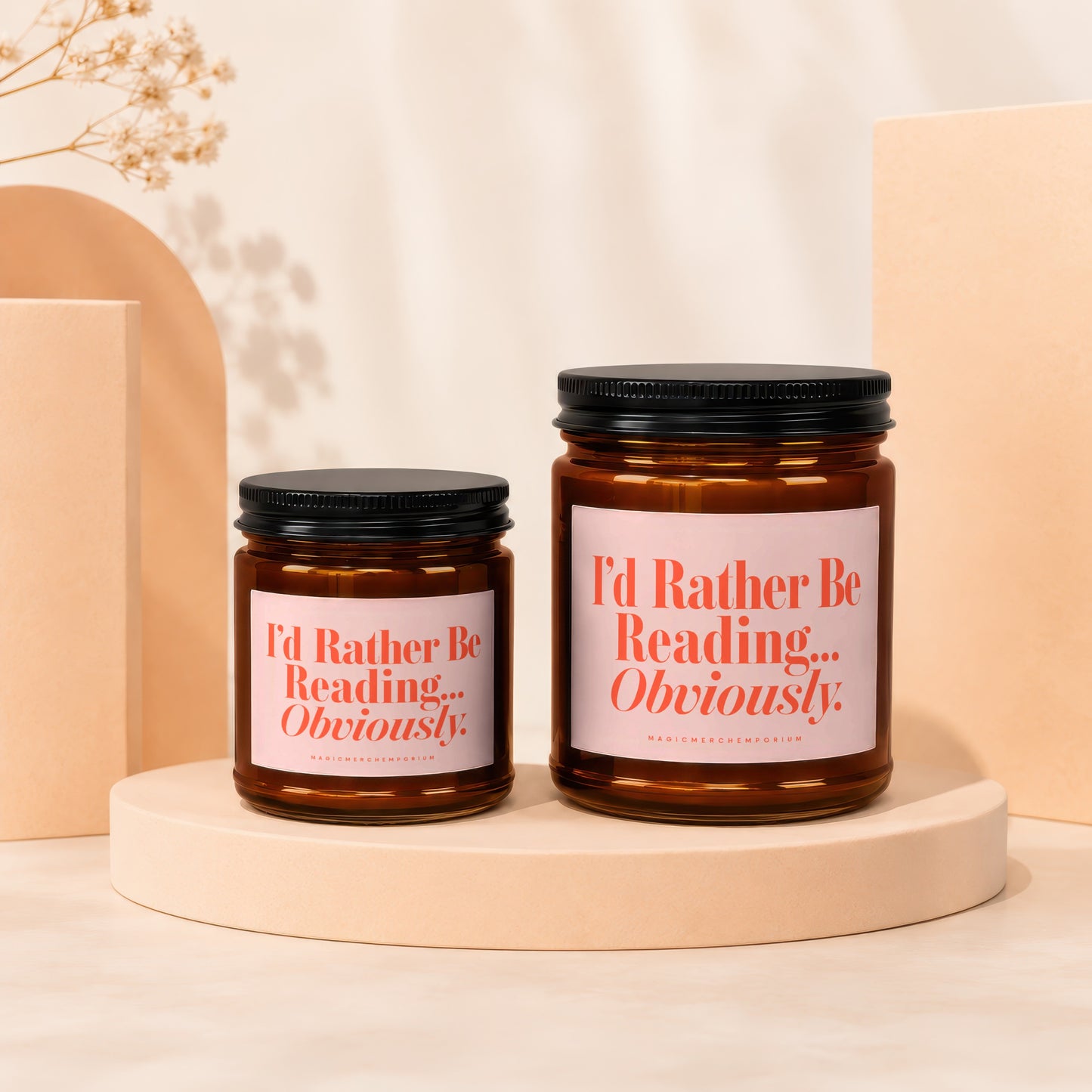 Two amber glass candles with black lids, each featuring a pink label with "I'd Rather Be Reading... Obviously." text.