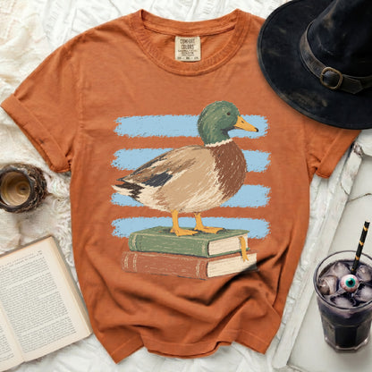 Orange t-shirt with a graphic of a duck standing on books.