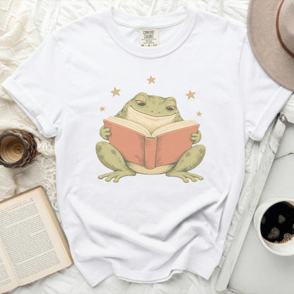 White t-shirt with a graphic of a contented frog reading a book.