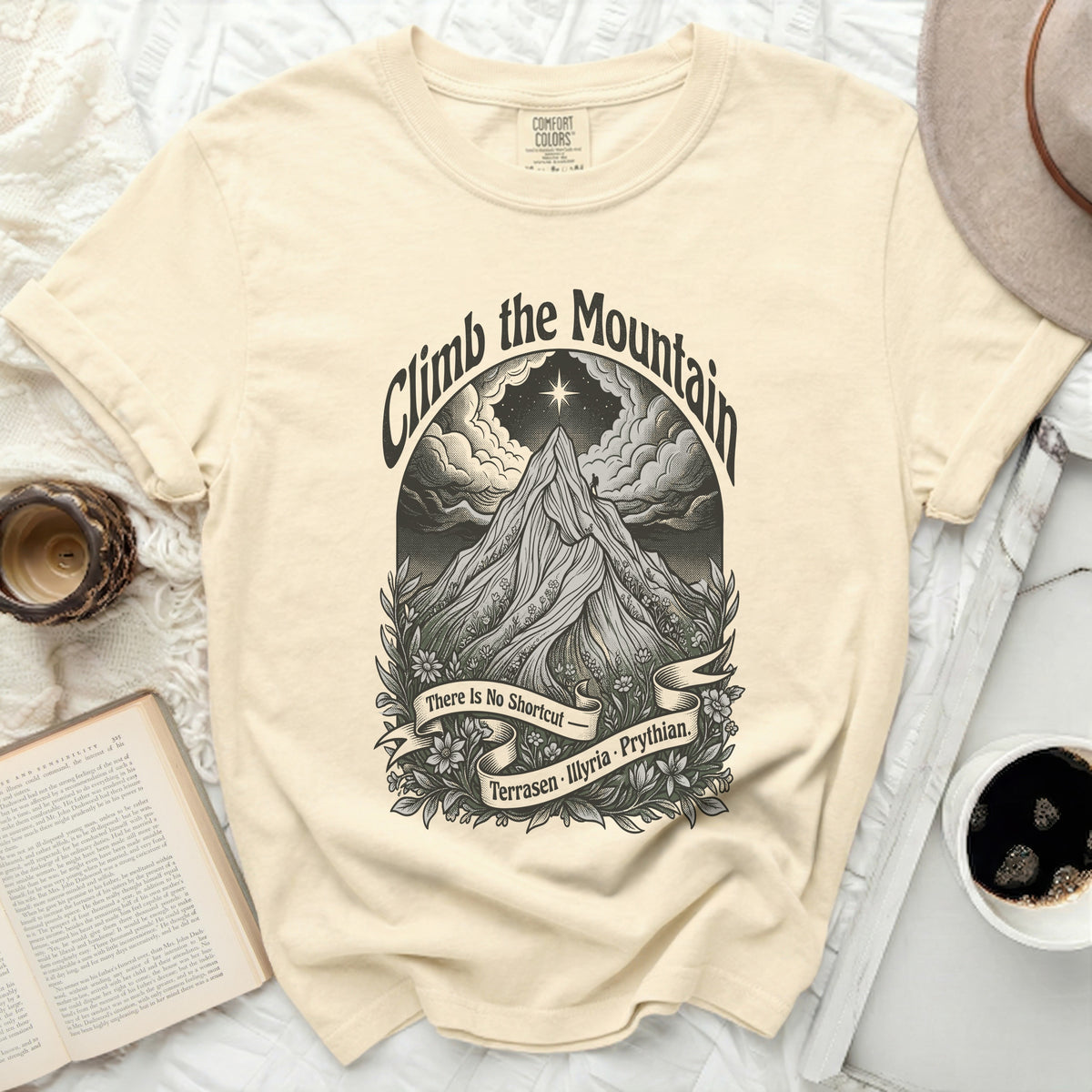 Cream t-shirt with "Climb the Mountain" graphic and text "There Is No Shortcut - Terrasen · Illyria · Phythian."