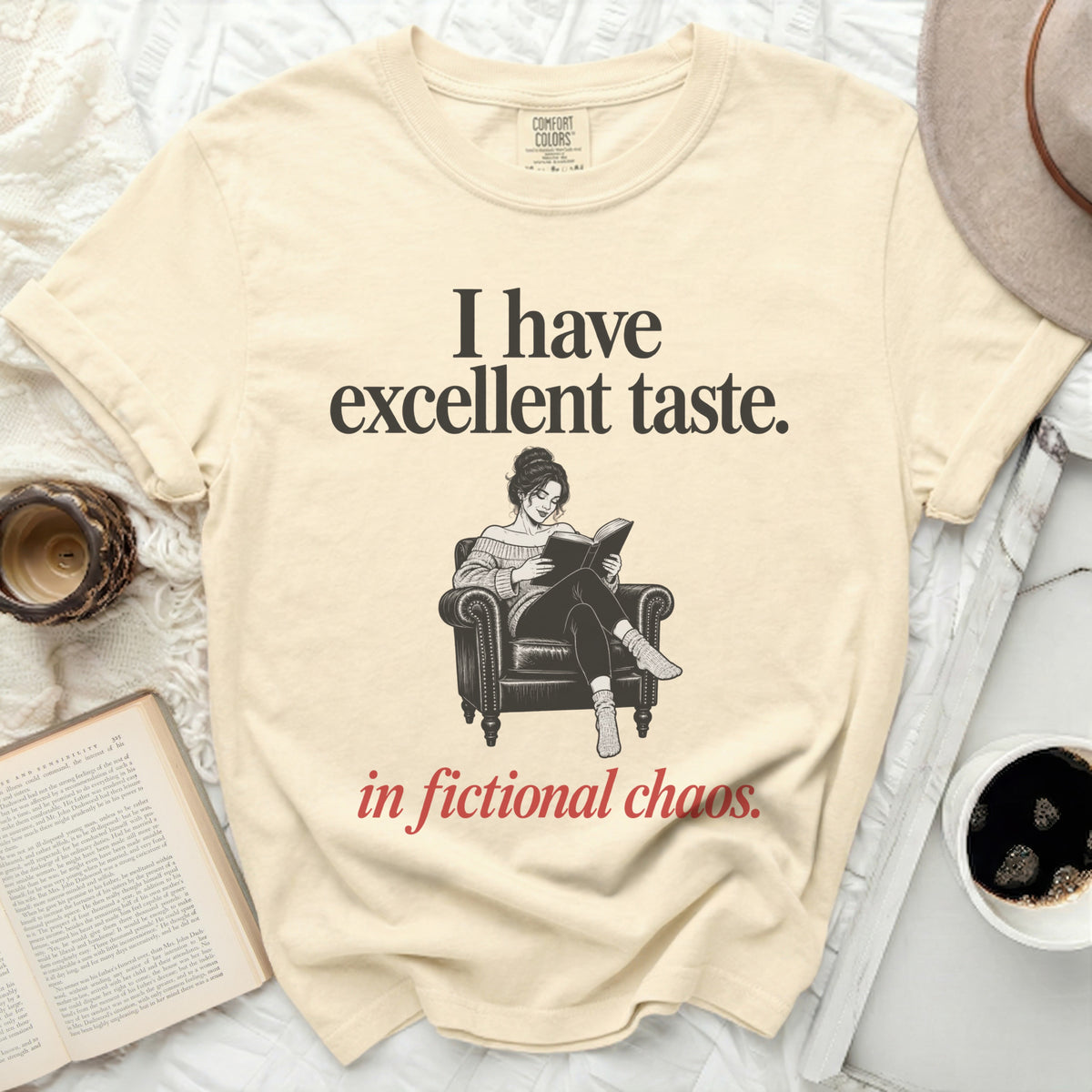 Cream t-shirt with "I have excellent taste. in fictional chaos." text and reading woman graphic.