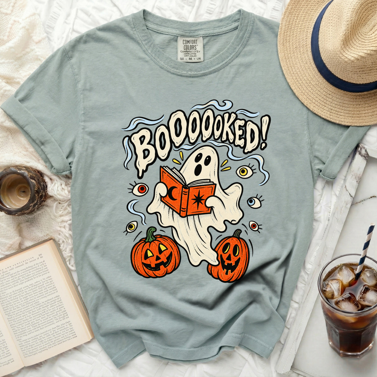 Ghost reading book with pumpkins, surrounded by eyes, and text "BOOOOOKED!"