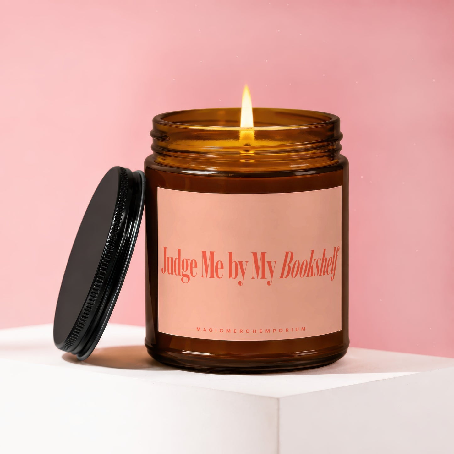 Brown glass candle with lit flame and lid next to it, "Judge Me by My Bookshelf" text.