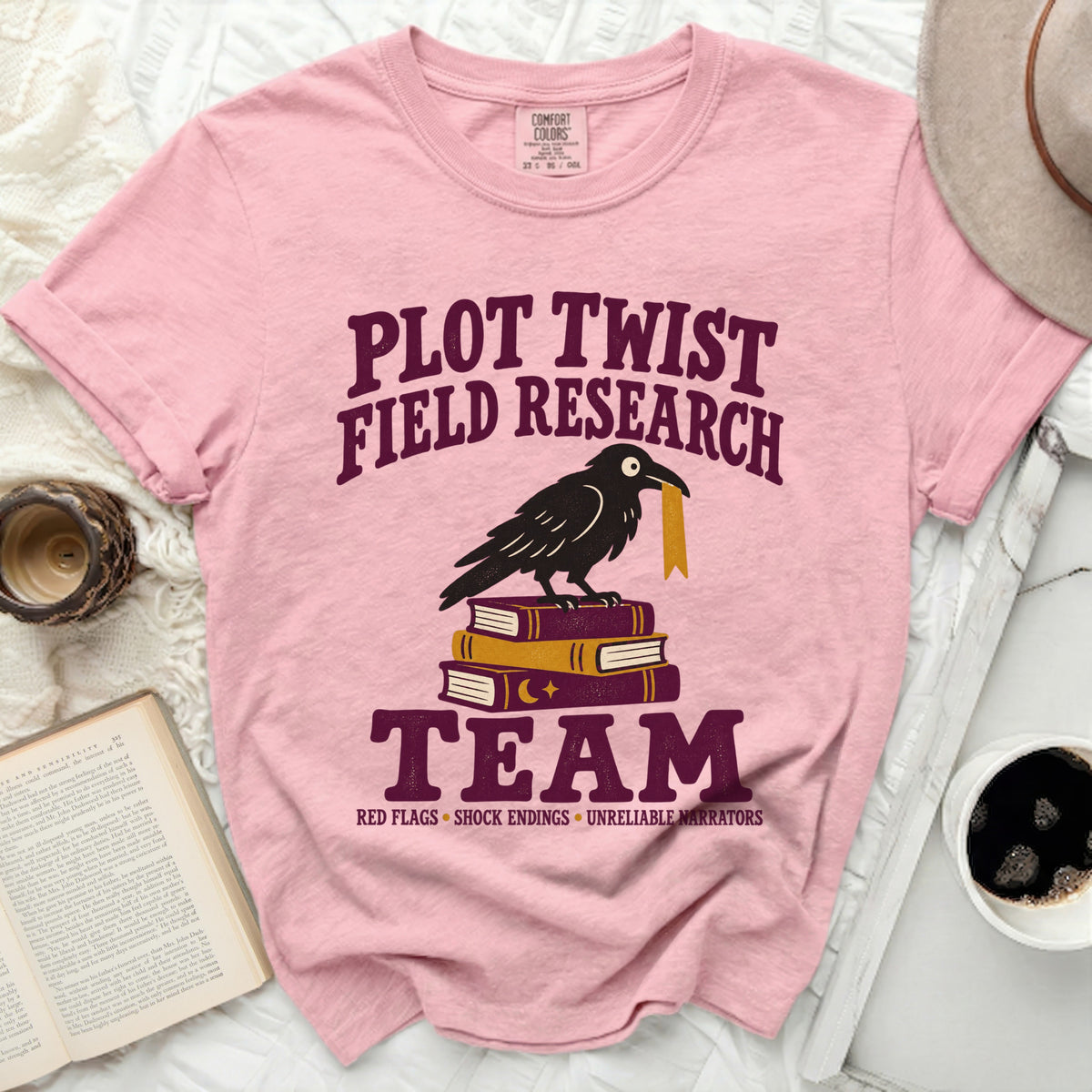Pink t-shirt with "Plot Twist Field Research Team" text and crow on books.