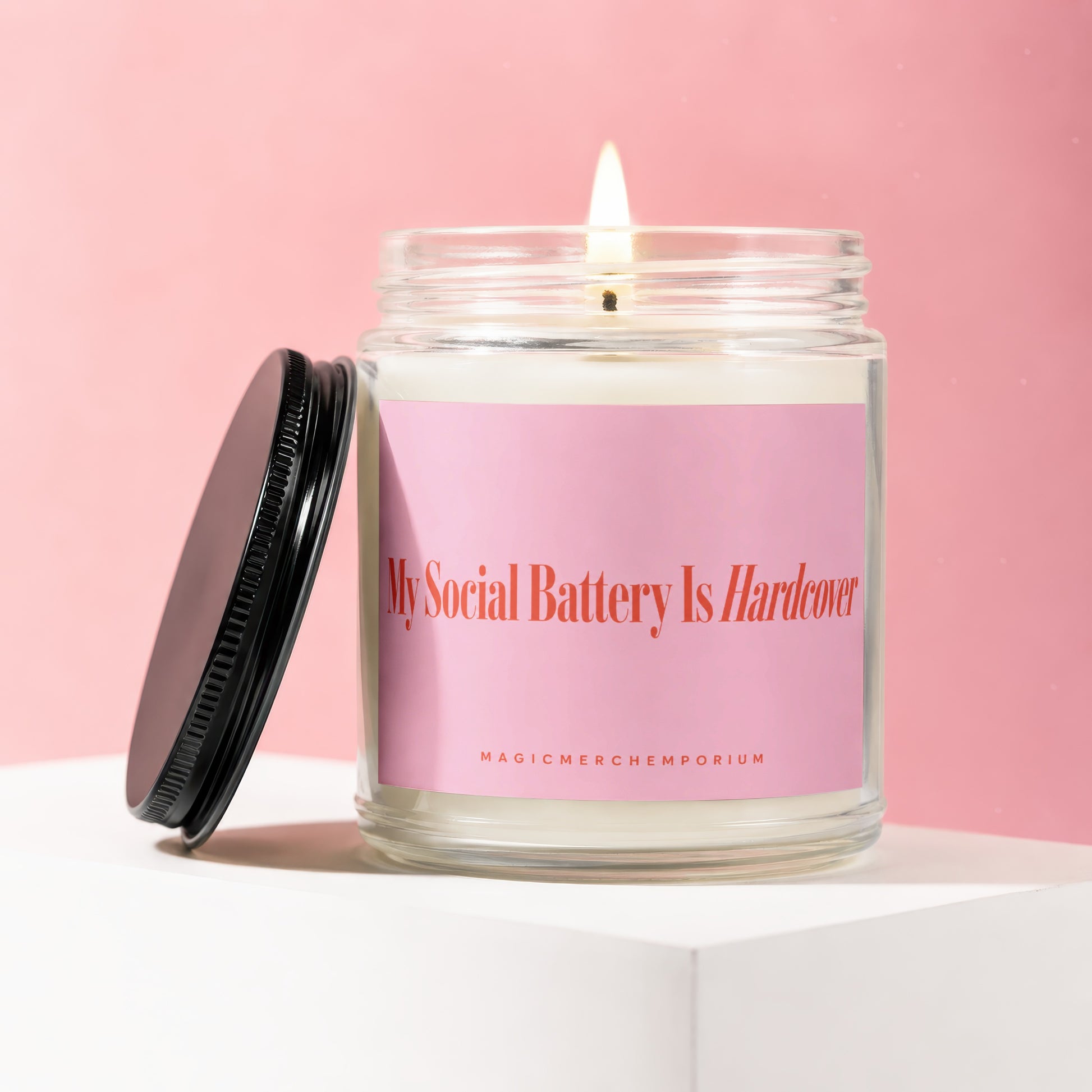 Candle with lit wick and pink label reading "My Social Battery Is Hardcover."