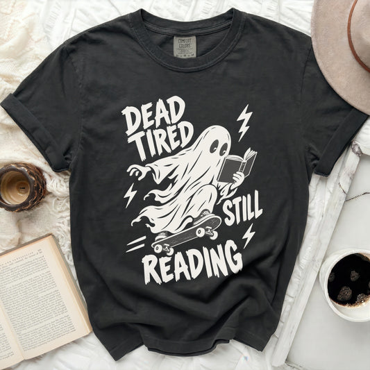 Black t-shirt with ghost on skateboard reading a book, "Dead Tired Still Reading."