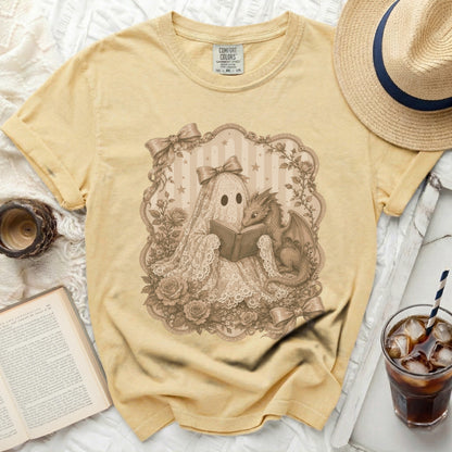 Yellow t-shirt graphic of a lace ghost and dragon reading a book.