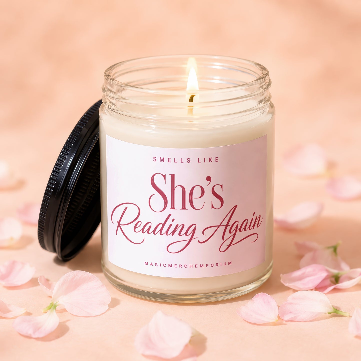 Candle with lit wick, a black lid, and a label that reads "She's Reading Again".