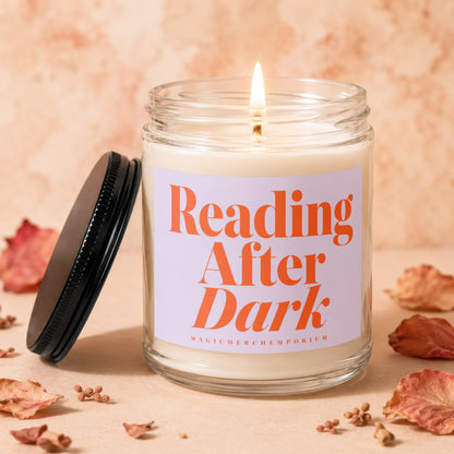 Lit glass jar candle with label "Reading After Dark" on a table with dried leaves.