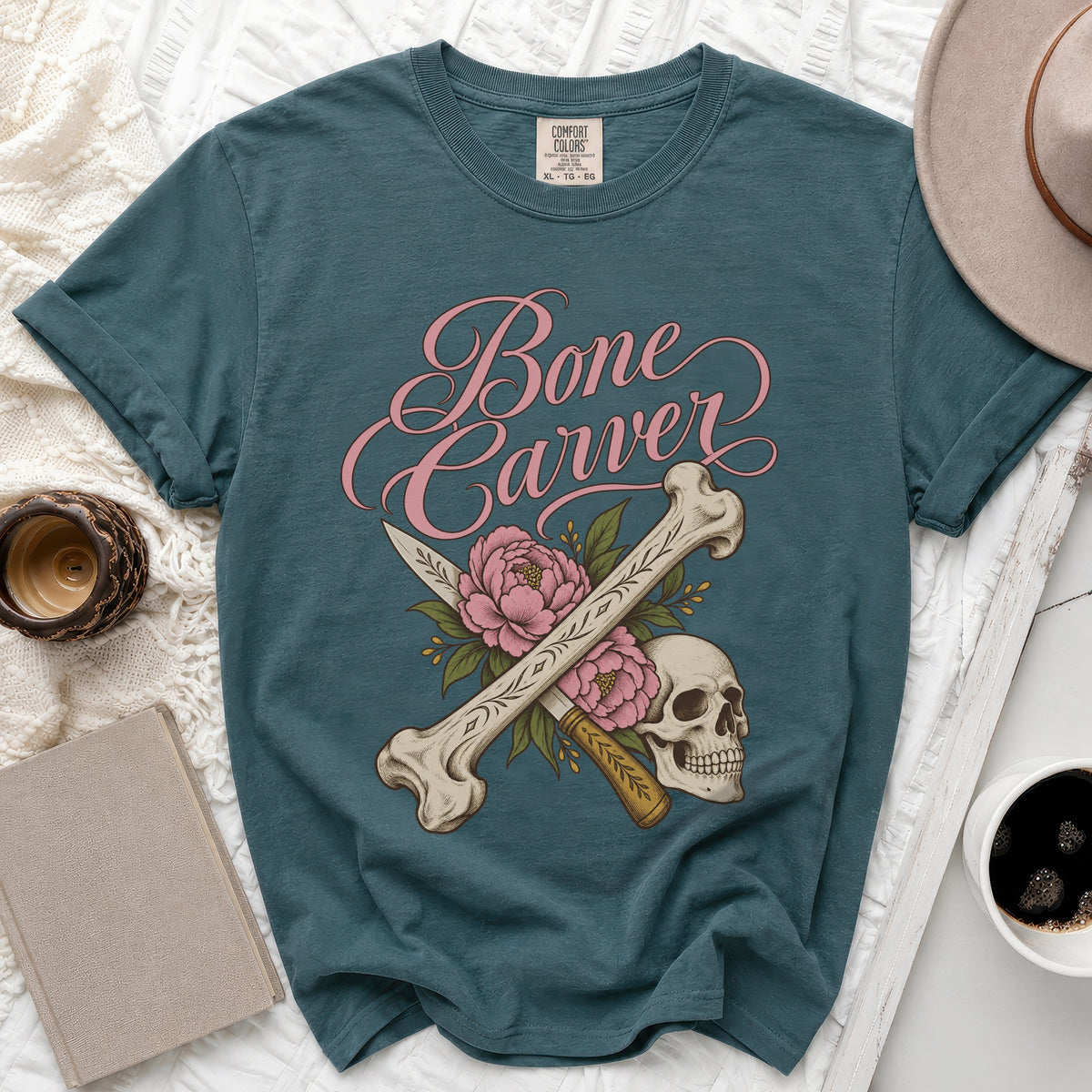 Teal t-shirt with "Bone Carver" text, skull, bones, knives, and pink flowers.