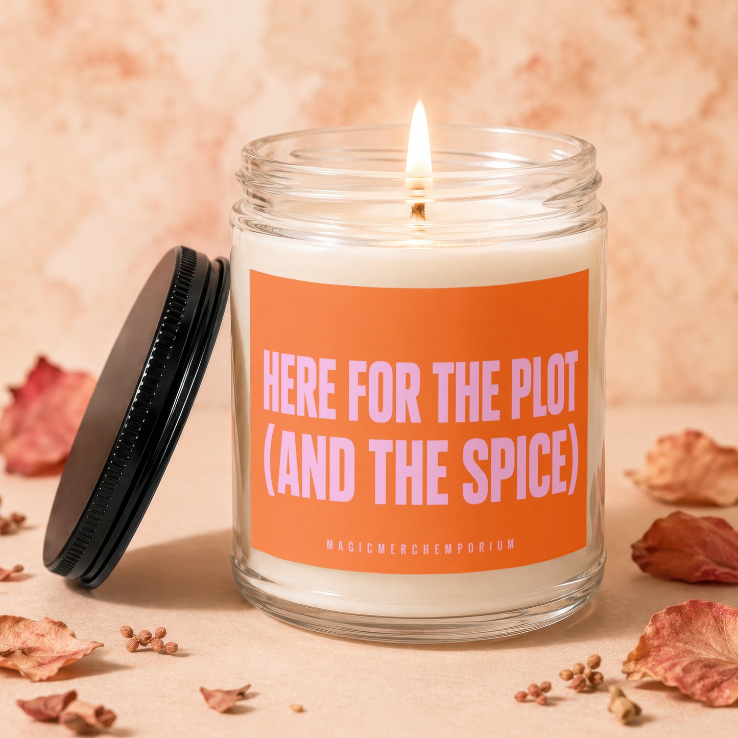Jar candle with lit flame and orange label reading "HERE FOR THE PLOT (AND THE SPICE)".
