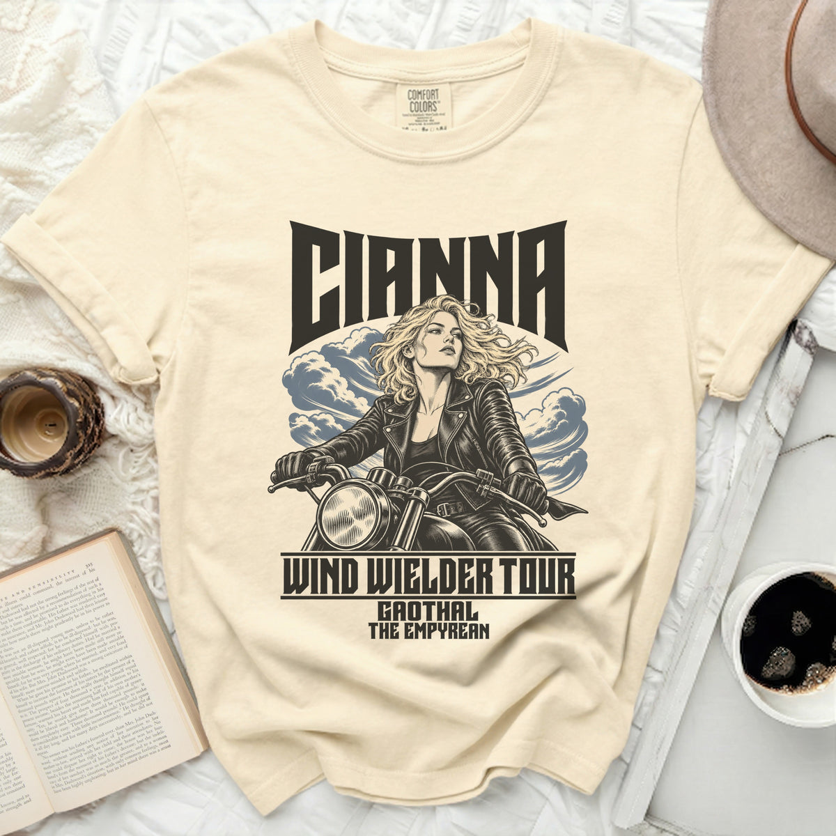 Cream t-shirt with graphic of woman riding motorcycle, text "CIANNA WIND WIELDER TOUR GAOTHAL THE EMPYREAN".