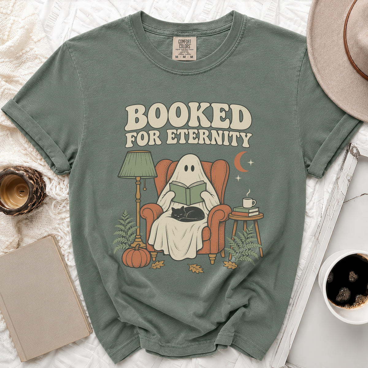 Ghost in armchair reading with cat, text "Booked for eternity", pumpkin, and moon.