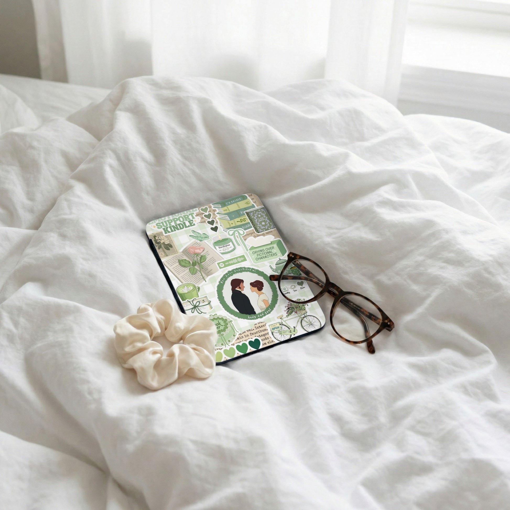 Kindle cover with "Support Kindle" and green book-themed stickers, next to glasses.
