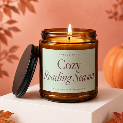 Amber glass candle with lit wick, lid off, labeled "Cozy Reading Season"