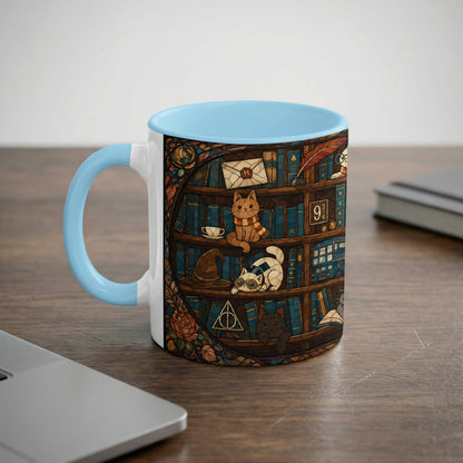 White mug with blue handle featuring a stained-glass design of cats on bookshelves.