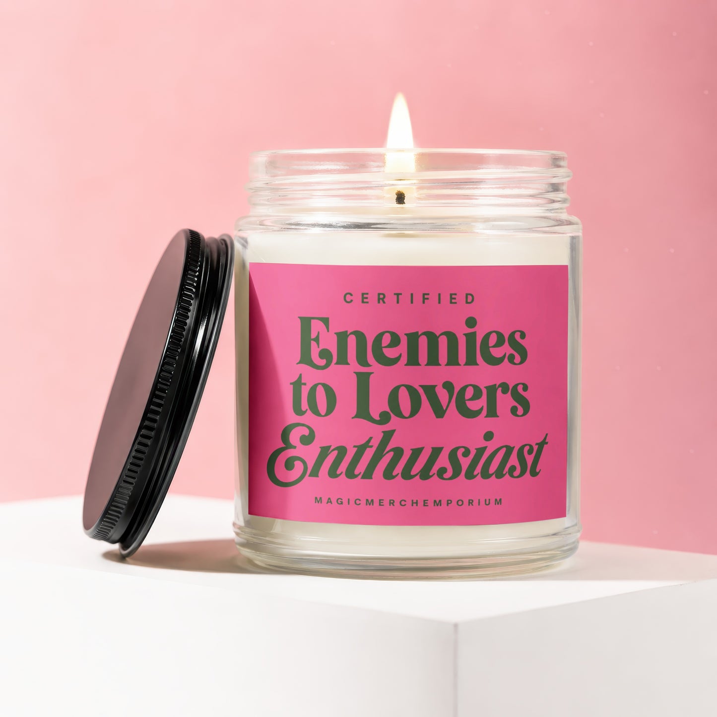 Glass jar candle with pink label "Certified Enemies to Lovers Enthusiast" on a pink background.