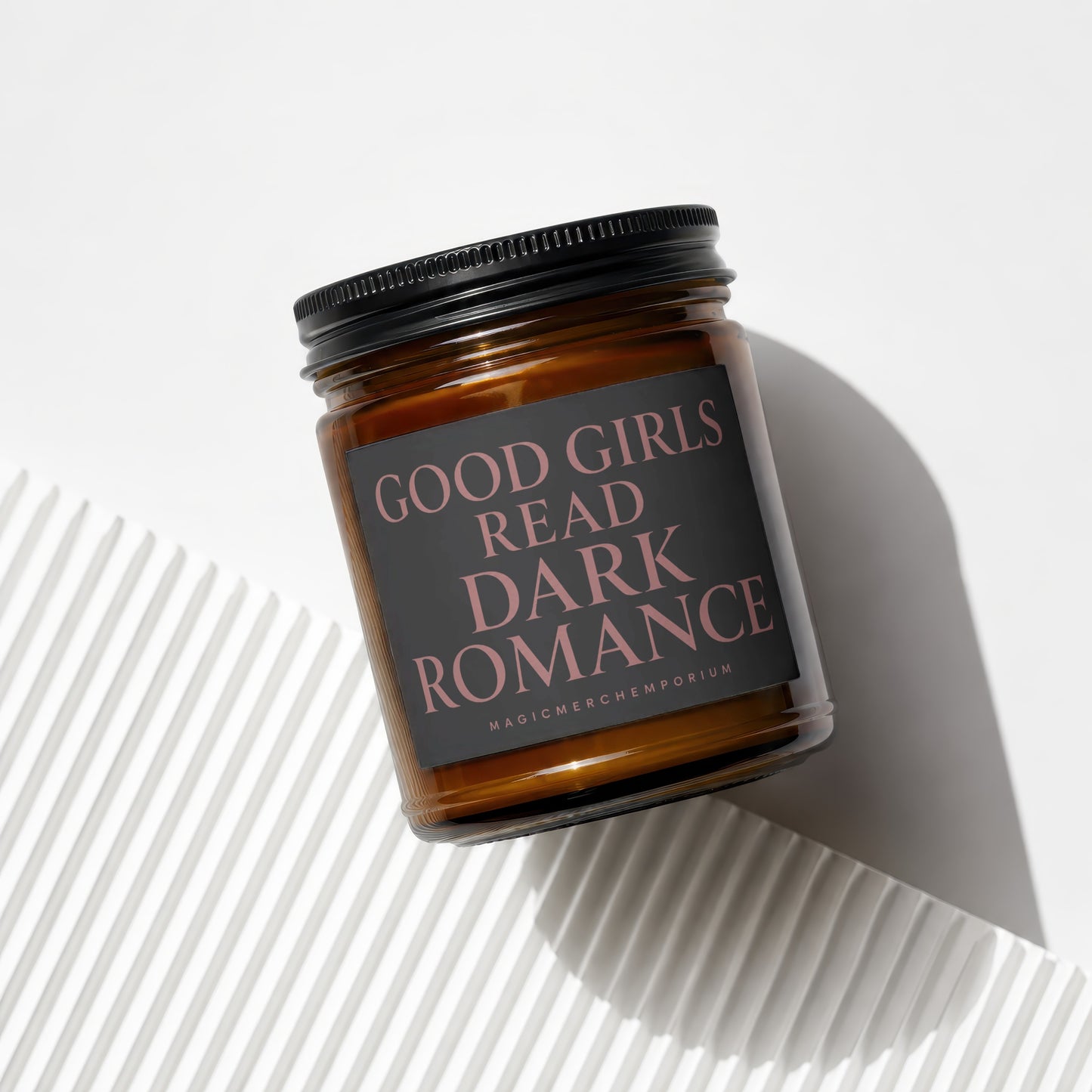 Amber glass candle with black lid and dark gray label reading "GOOD GIRLS READ DARK ROMANCE".